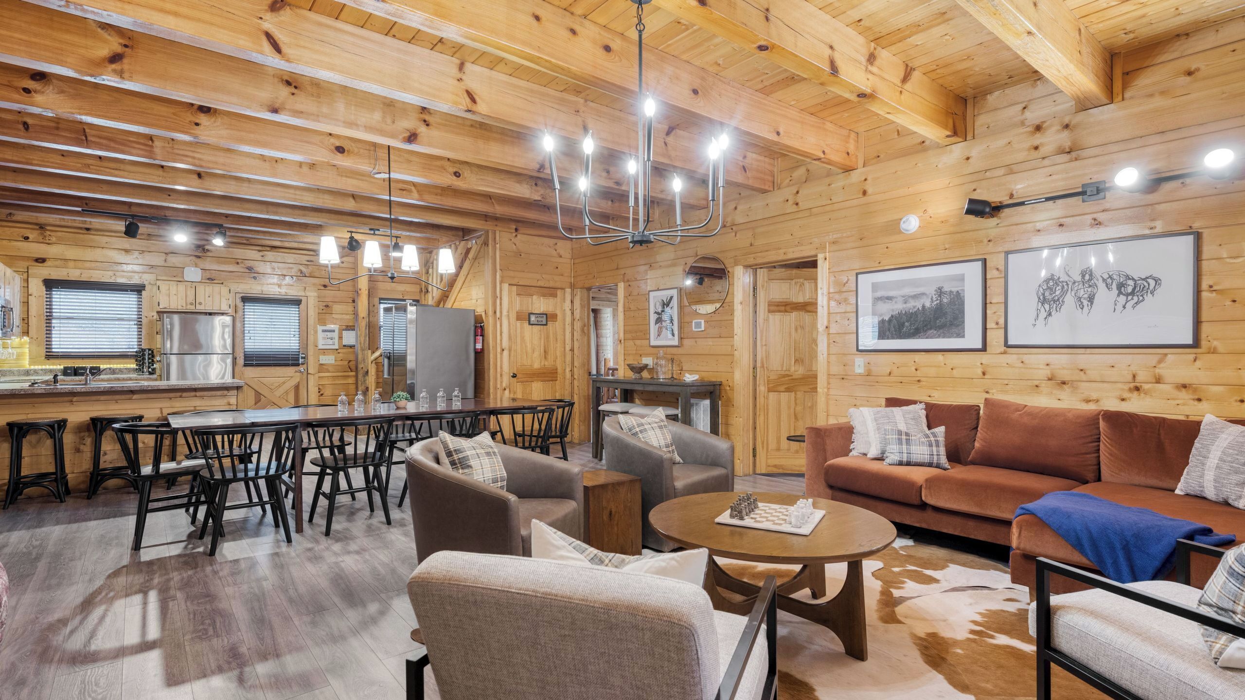 A wooden cabin interior with a dining area, kitchen, and seating area.