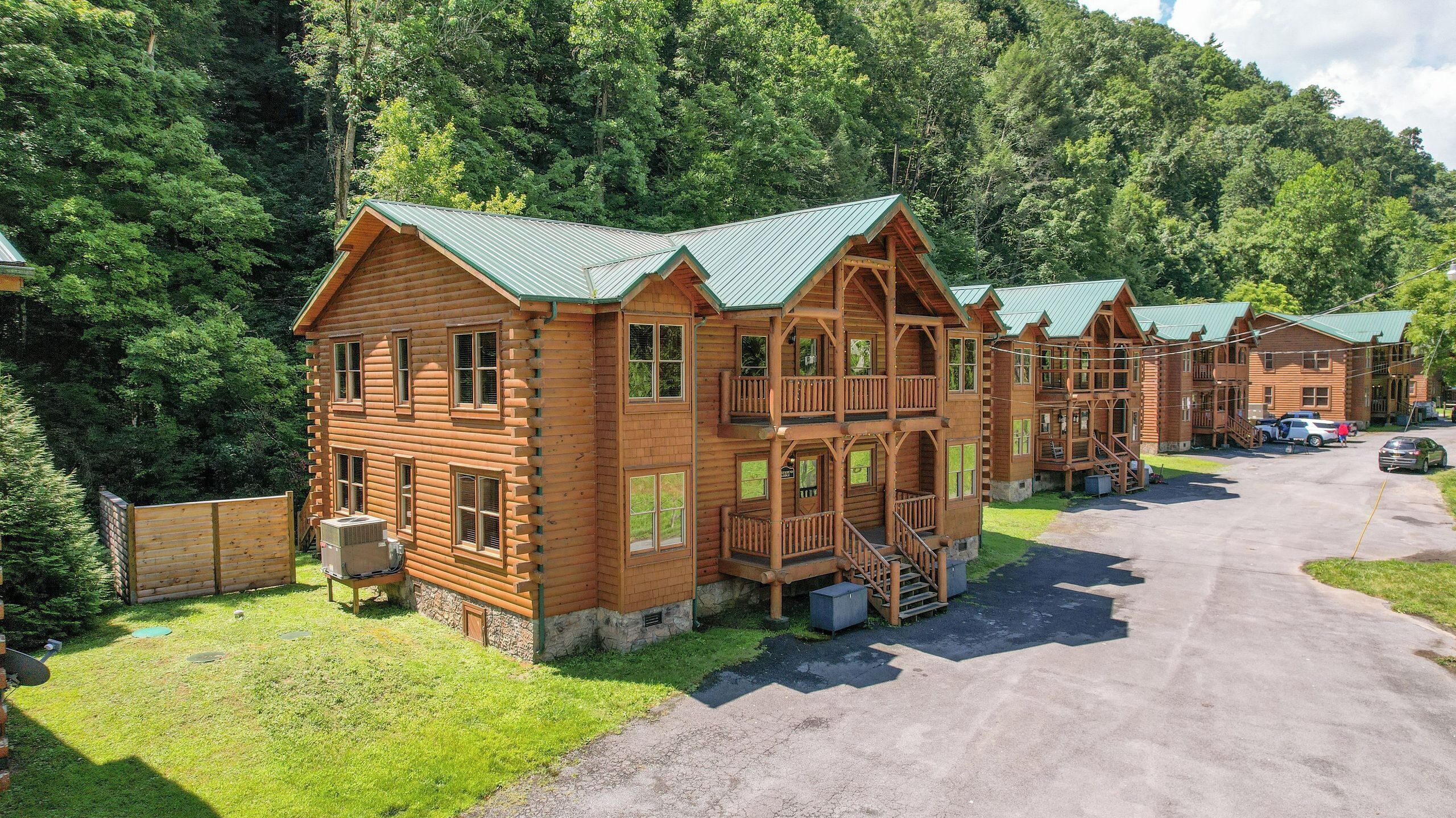 A row of log cabins with multiple stories and balconies, surrounded by a forested area.