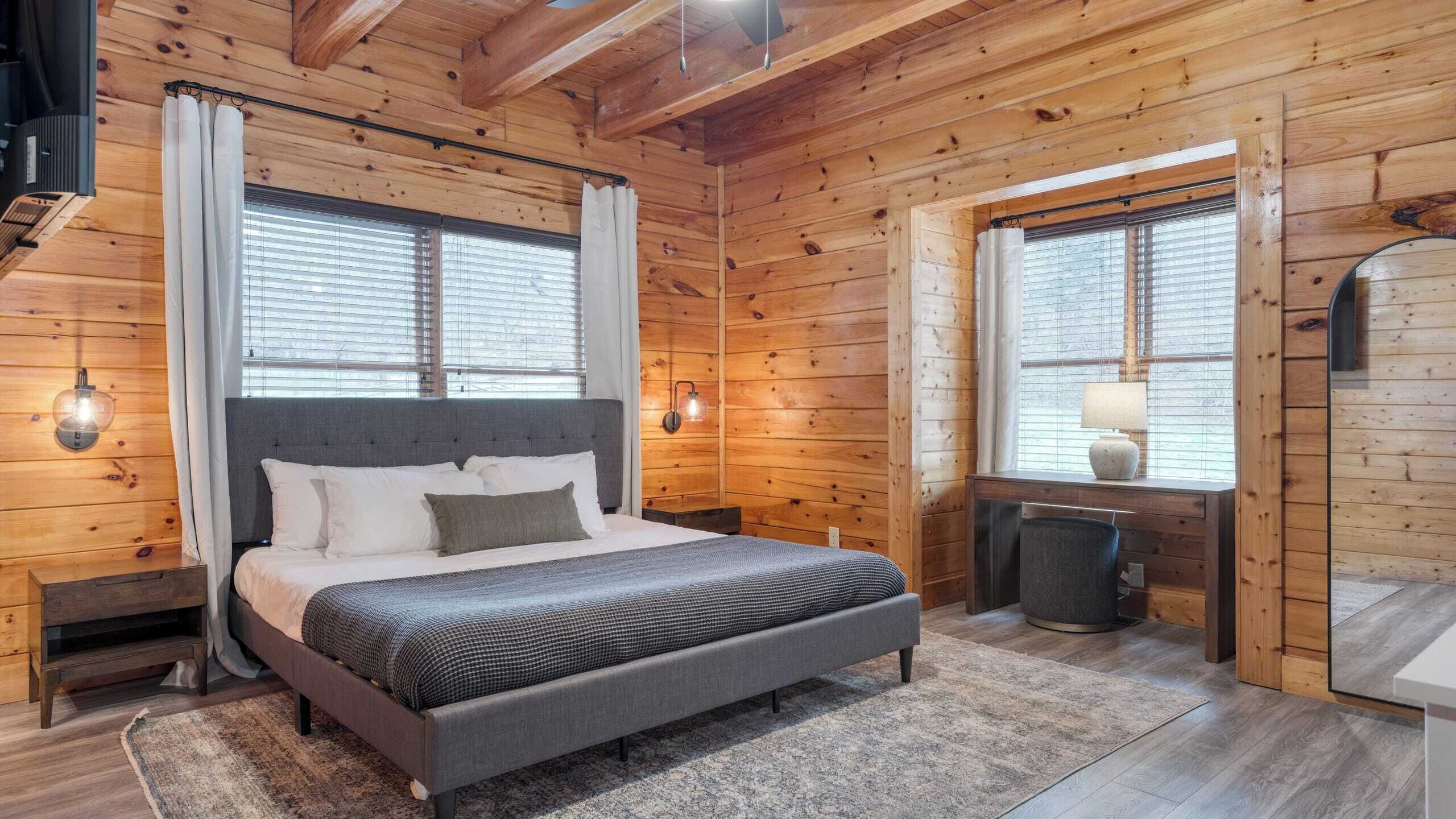 A wooden cabin bedroom with a bed, bedside tables, a desk, and a chair.
