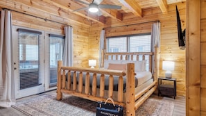 Quarto de cabana de madeira com uma cama, duas luminárias de cabeceira, um ventilador de teto e vista pelas janelas.