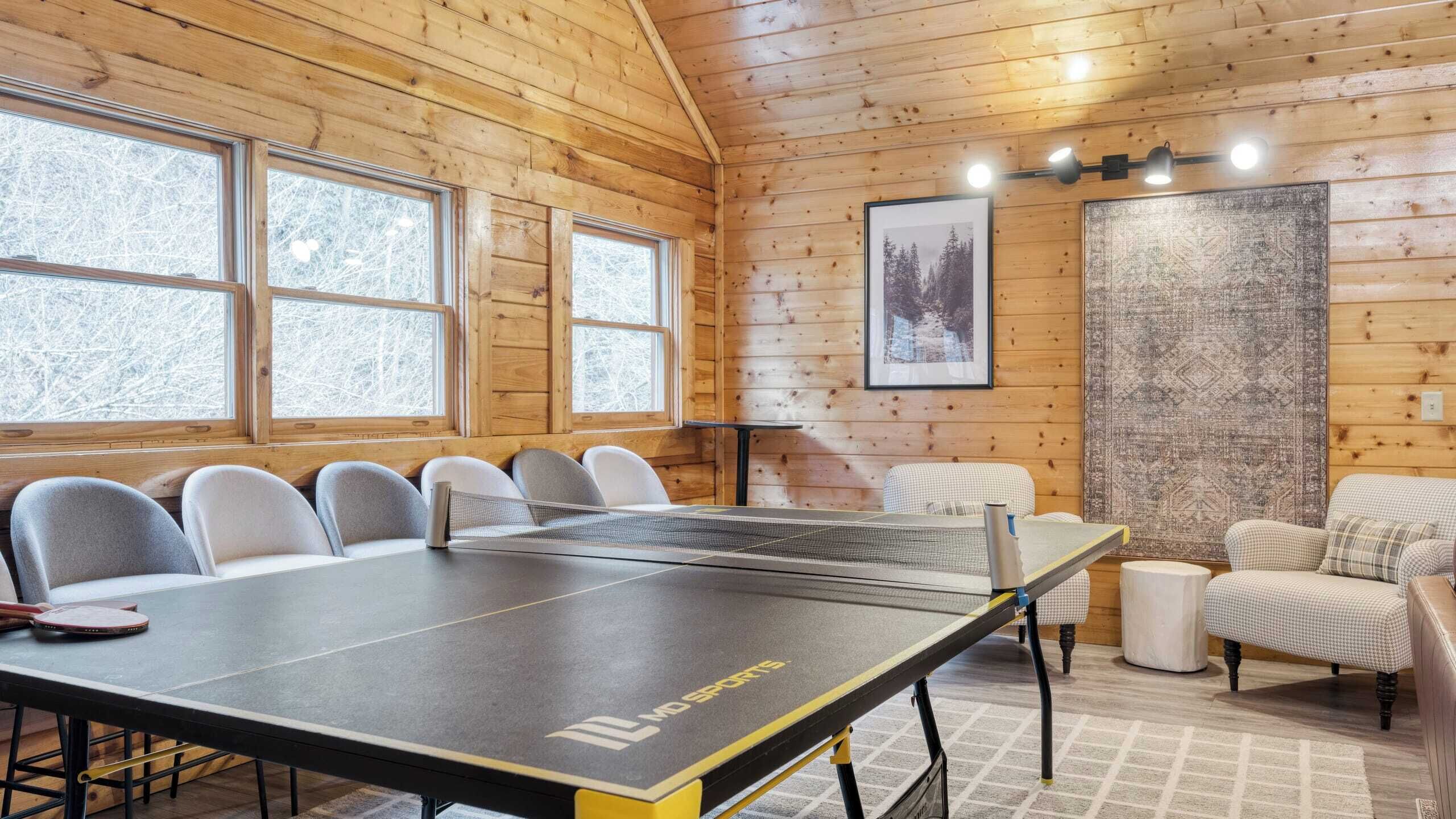 A room with a ping pong table, chairs, a small table, and a couch.