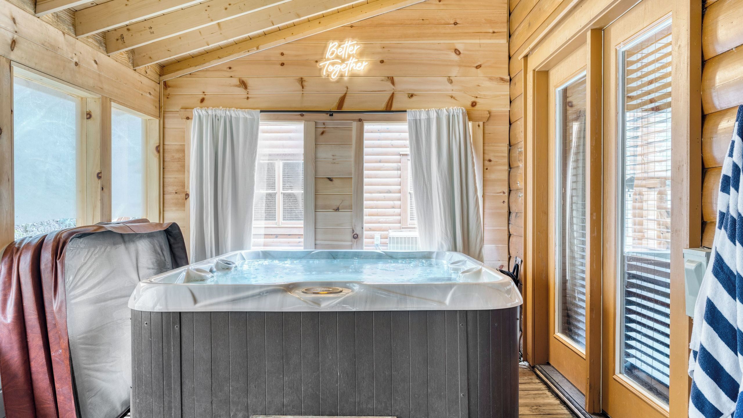 A wooden cabin interior with a hot tub, large windows, and curtains.