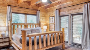 A wooden cabin bedroom with a bed, curtains, and framed pictures on the walls. - Brookshore by Avantstay Relaxing Backyard Creek, 10mins From Pigeon Forge (Pigeon Forge)