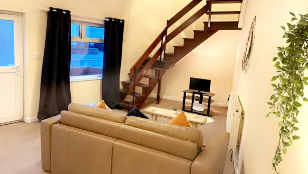 A living room with a beige sofa, a small table, a TV, and a staircase.