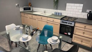 A modern kitchen with a glass dining table, chairs, a microwave, sink, stove, and cabinets.