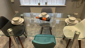A dining area with a glass table, four chairs, and a bottle of wine.