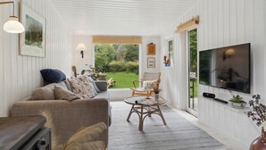 A cozy living room with a sofa, armchair, and coffee table, a TV mounted on the wall, and a view of a garden through a large window. - Beautiful home in Vig with WiFi (Vig)