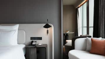 Una habitación de hotel moderna con una cama, un escritorio con teléfono, una lámpara, un sofá y una ventana con cortinas.