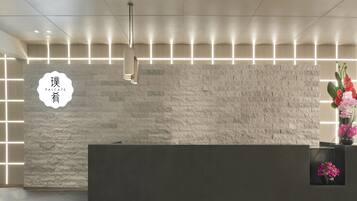 A reception desk with a stone-textured wall, a modern pendant light, and a vase with flowers.