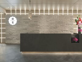 A reception desk with a stone-textured wall, a modern pendant light, and a vase with flowers.