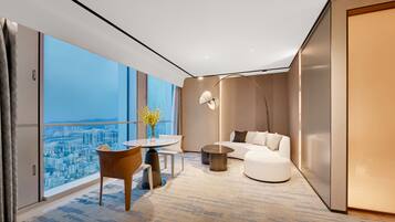 Habitación de hotel moderna con vistas a la ciudad, una mesa redonda, un sofá y una lámpara de pie.