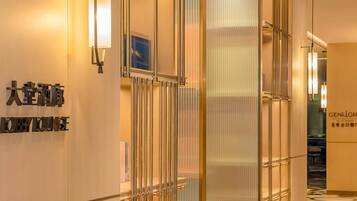 Vestíbulo de hotel con diseño moderno, que incluye una recepción, un amplio separador de vidrio y un letrero que indica el área de estar del vestíbulo.