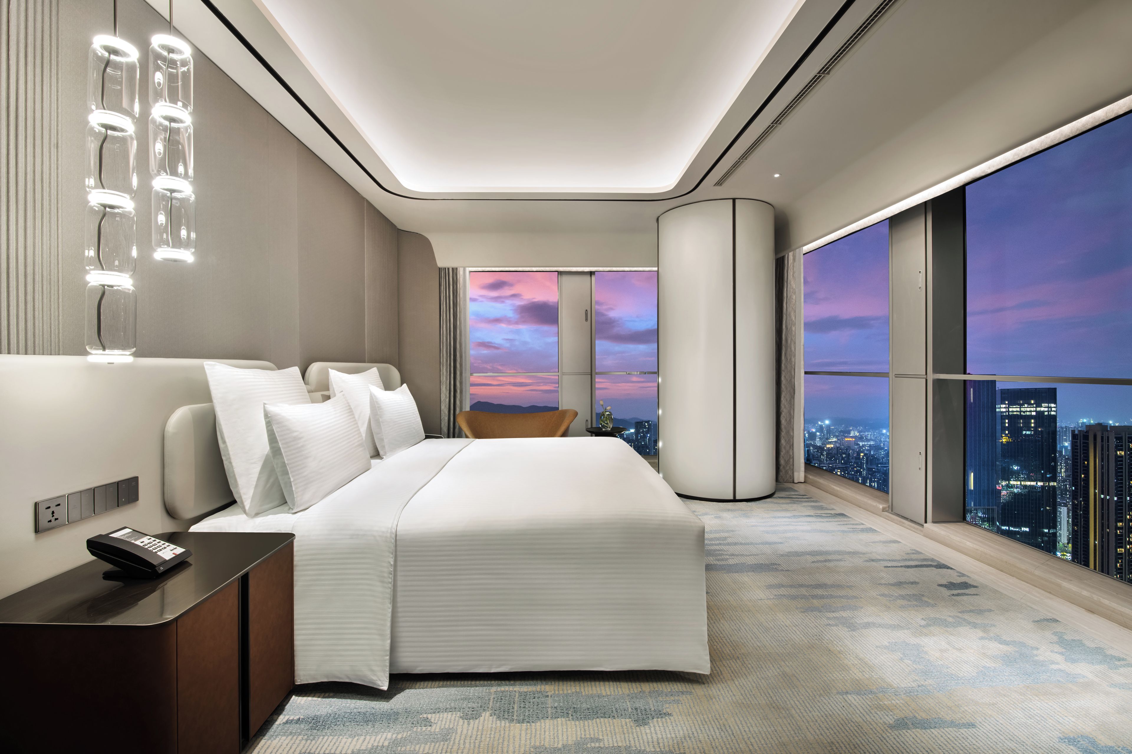 A modern hotel room with a large bed, a nightstand, a remote control, and a city view through the window.