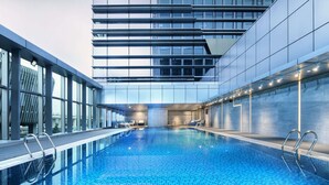 Une piscine int érieure moderne avec des parois en verre transparent, un sol carrelé et un espace détente comprenant des chaises et une table.