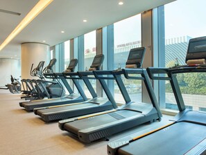 A row of treadmills in a gym with large windows and a view of a building.