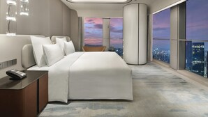 Une chambre d’hôtel moderne avec un grand lit, une table de chevet avec une télécommande, une chaise et une grande fenêtre donnant sur la ville.