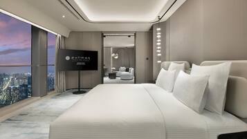 A modern hotel room with a large bed, a television, a city view, and a separate seating area.