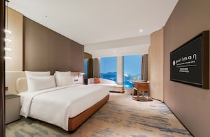 A hotel room with a large bed, a desk, a chair, and a TV on the wall.