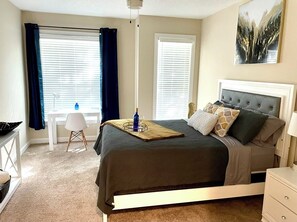 Cozy bedroom with a neatly made bed, nightstand, desk, and large window.