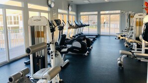 Un gimnasio con equipo de ejercicio, ventanas amplias y un ventilador de techo.