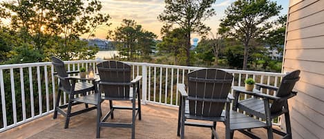 A covered outdoor area with two Adirondack chairs and a table, overlooking a body of water and trees.