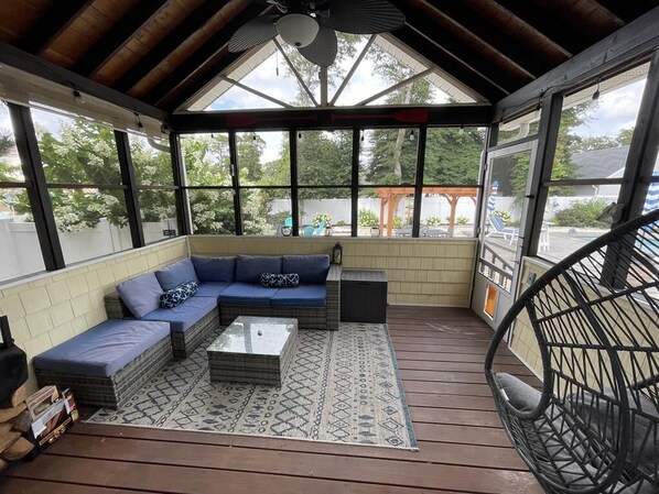 A covered patio area with a sectional sofa, a coffee table, and a hanging chair.