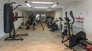Een fitnessruimte met diverse trainingsapparaten, waaronder een bokszak, hometrainers en krachtapparaten.