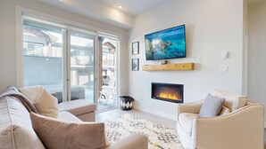 Una sala de estar moderna con chimenea, un televisor grande y un balcón con puertas de vidrio.
