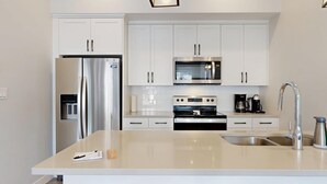 Una cocina moderna con armarios blancos, electrodomésticos de acero inoxidable, microondas integrado, cafetera y lavabo.