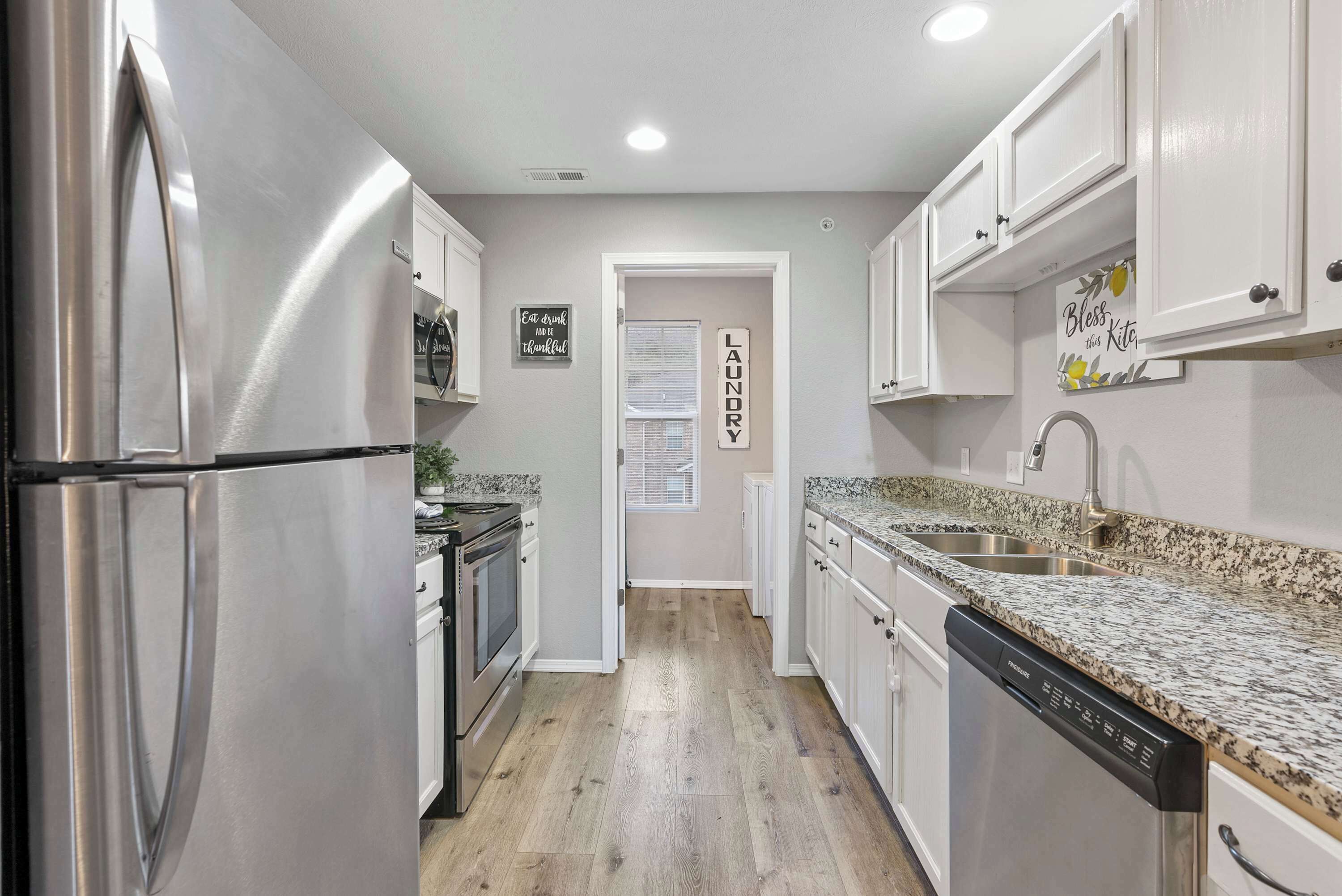 Una cocina moderna con electrodomésticos de acero inoxidable, encimeras de granito y armarios blancos.