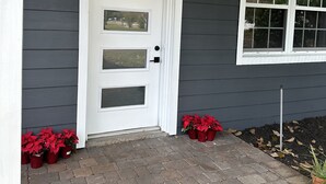 A house with a white front door, a window with white trim, and red poinsettia plants on the ground.