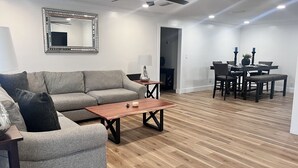 A modern living room with a grey sofa, wooden coffee table, and a dining area with a dark wooden table and chairs.