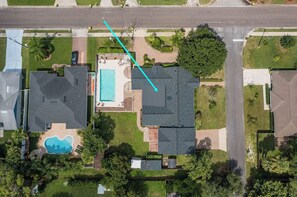 An aerial view of a residential area with a swimming pool, a tennis court, and a driveway.