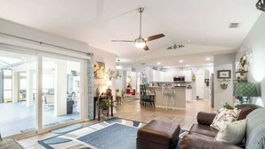 A spacious living room with a large window, a ceiling fan, and a kitchen in the background. - 25%off/Close to Disney/Hot Tub/Private Pool/Fenced (Davenport)