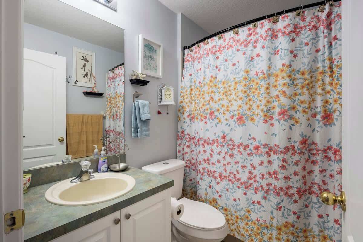 Een badkamer met een douchegordijn met bloemenprint, een wastafel, een toilet en een spiegel.