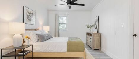 A bedroom with a bed, bedside tables, a ceiling fan, a window, and a dresser.