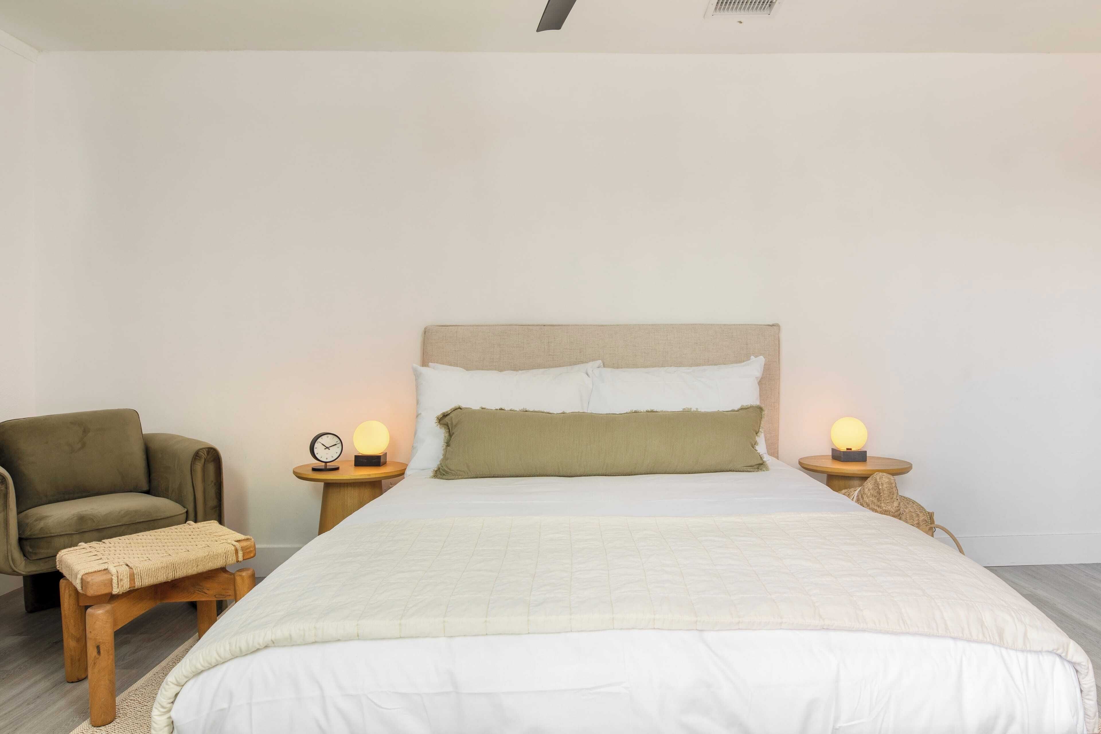 Une chambre à coucher avec un lit, deux tables de chevet avec des lampes, une chaise et un banc.