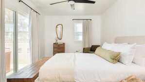 A bedroom with a large bed, a ceiling fan, a wooden bench, a dresser, and a window with curtains. - Boho Joshua Tree Escape w/ Firepit, Courtyard & Epic Views Asteroid by Avantstay (Twentynine Palms)