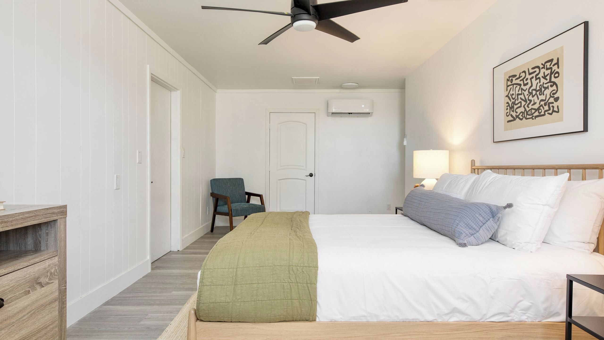 A bedroom with a bed, a chair, a ceiling fan, and a wall-mounted air conditioner.