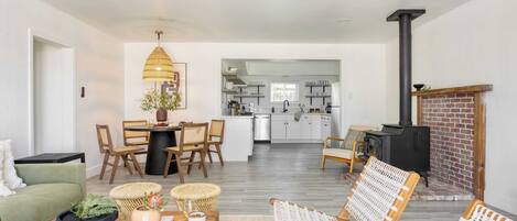 A modern living room with a dining area, a kitchen in the background, and a fireplace.