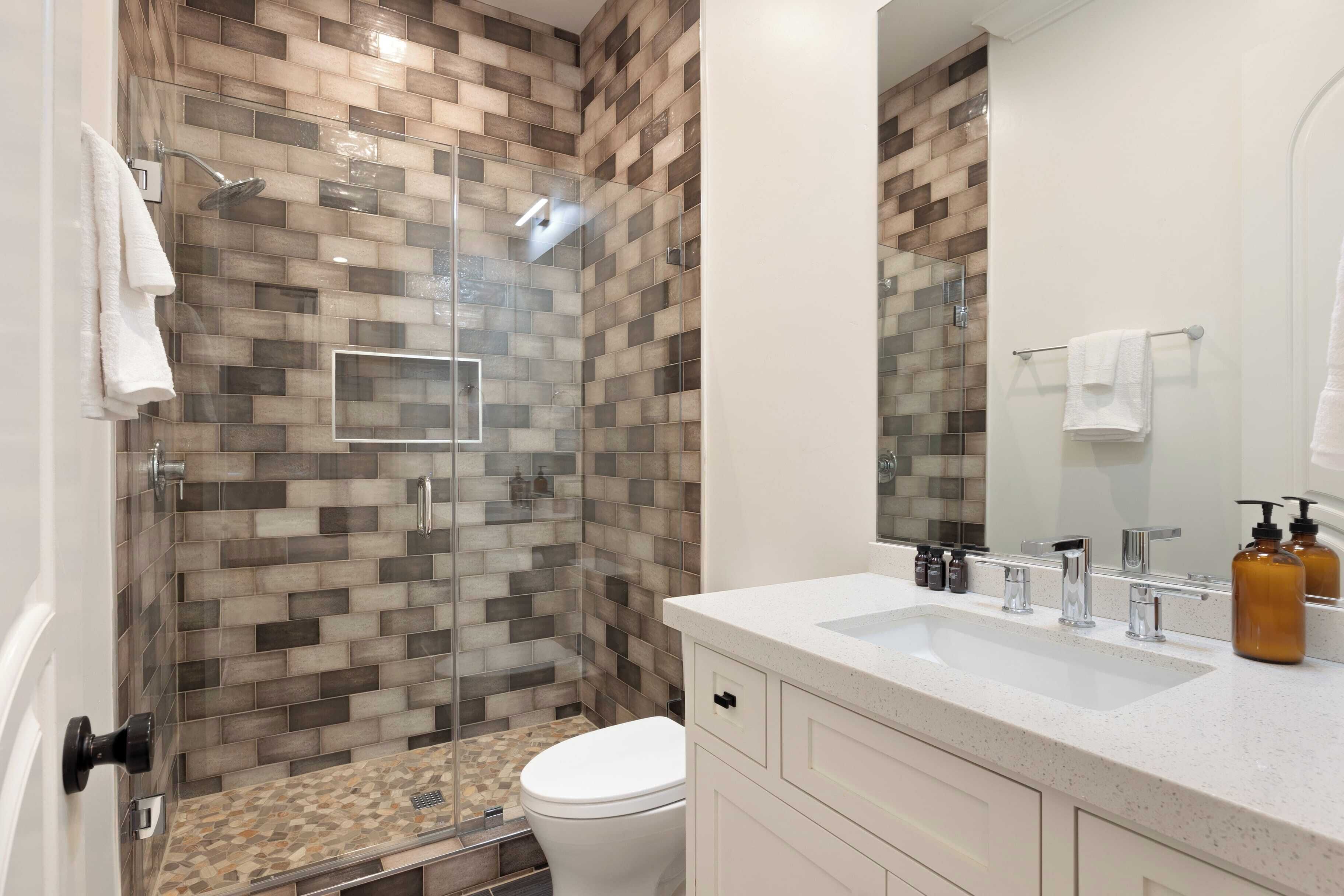 A modern bathroom with a glass-enclosed shower, a white toilet, and a vanity with a mirror and sink.