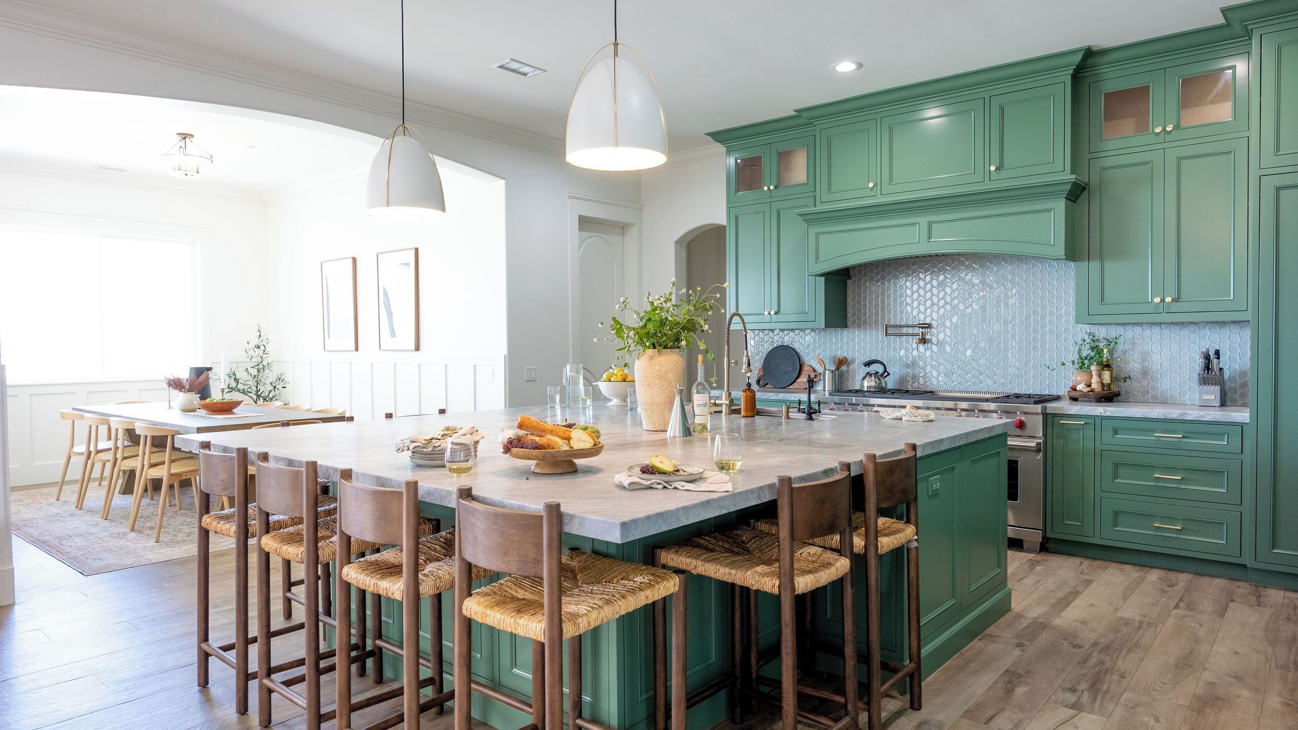A spacious kitchen with green cabinets, a central island with bar stools, and a dining area with wooden chairs.