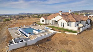 Ein modernes, zweistöckiges Haus mit Swimmingpool, einer Terrasse mit Liegestühlen und Blick auf die umliegende Landschaft.