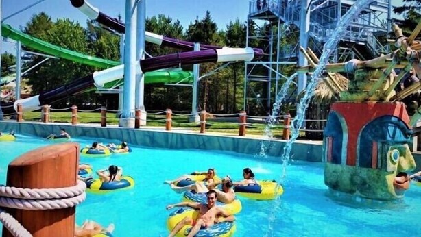 Un parque acuático con área de piscina, toboganes y una gran fuente de agua.