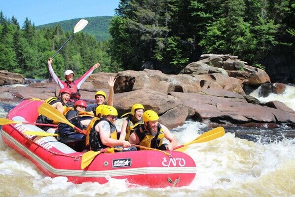 Un grupo de personas en un bote inflable rojo navegando por un río rodeado de rocas y árboles.