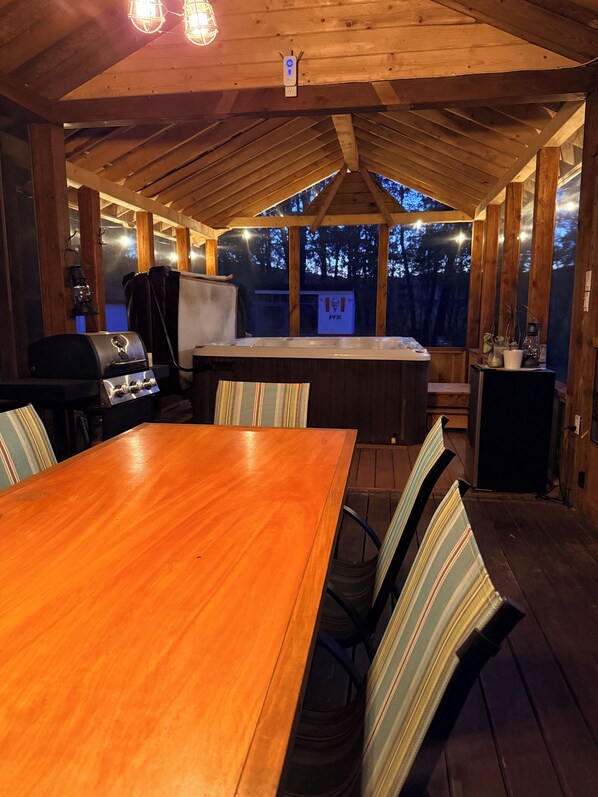 A wooden deck with a table and chairs, a grill, and a hot tub.
