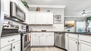A modern kitchen with white cabinets, stainless steel appliances, and a wooden floor. - 2-Minute Walk to the Beach + Pool Views! (Corpus Christi)