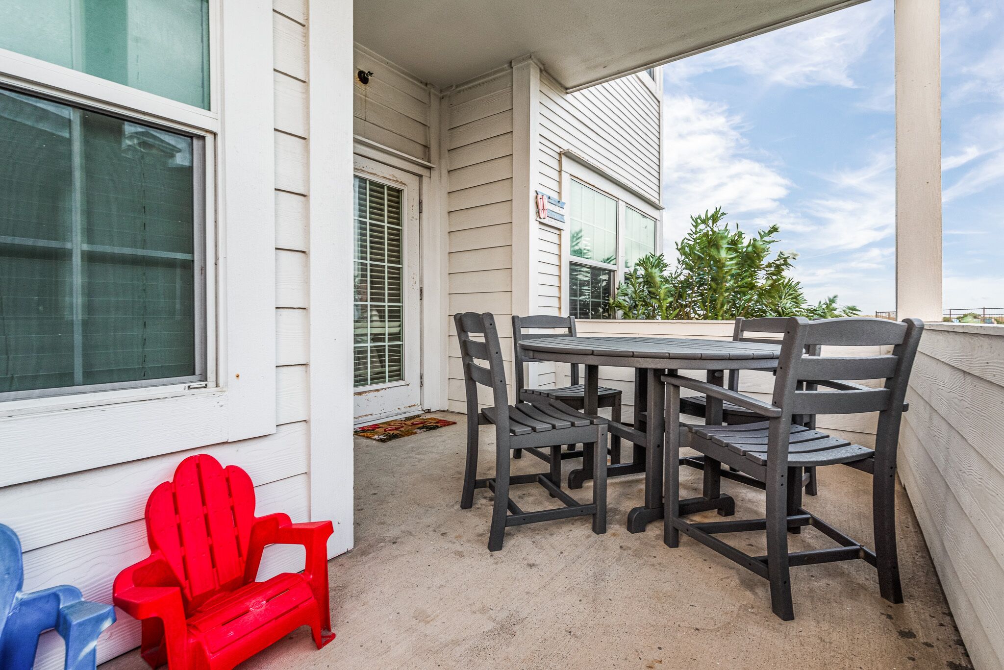 A patio with a table and chairs, a red Adirondack chair, and a blue Adirondack chair.
