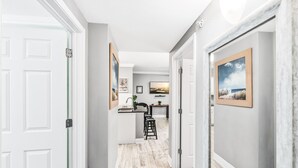 A hallway with a kitchen area, featuring a counter, stools, and framed artwork on the walls. - 2-Minute Walk to the Beach + Pool Views! (Corpus Christi)