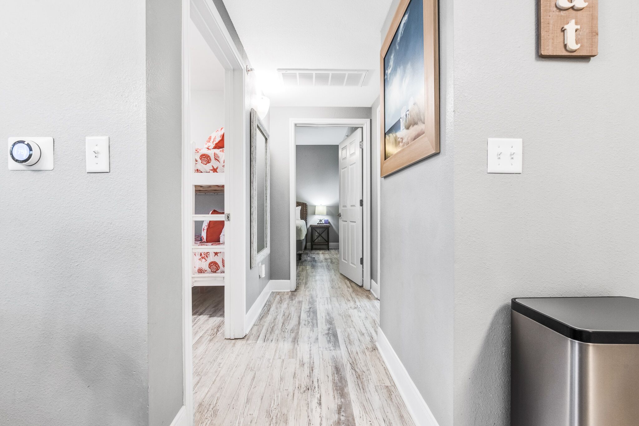 Un couloir avec un plancher en bois, des murs blancs et une poubelle sur le côté droit.
